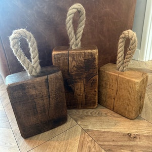 Puede incluir: Tres topes de puerta de madera rústica con asas de cuerda. Los topes de puerta están hechos de madera recuperada y tienen un acabado natural y desgastado.