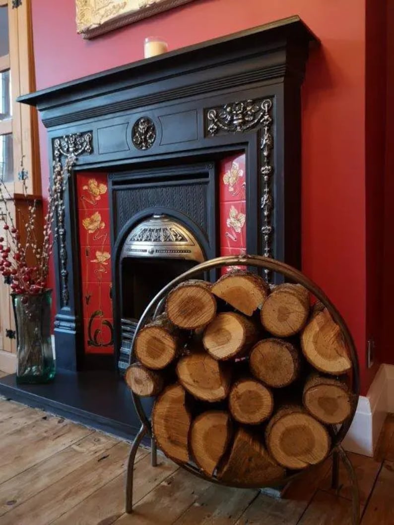 Puede incluir: Una chimenea de metal negro con un marco de azulejos rojos y blancos. Un porta-le&ntilde;a redondo de metal con troncos apilados se encuentra frente a la chimenea.