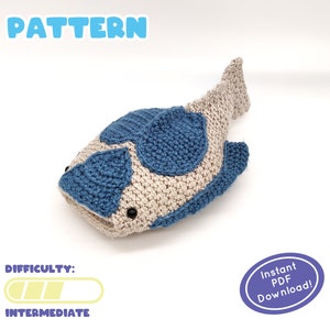 May include: A crocheted fish pattern in beige and blue. The fish has blue spots and black button eyes. The word "PATTERN" is at the top in blue, and "DIFFICULTY: INTERMEDIATE" is at the bottom. An oval sticker says "Instant PDF Download!"