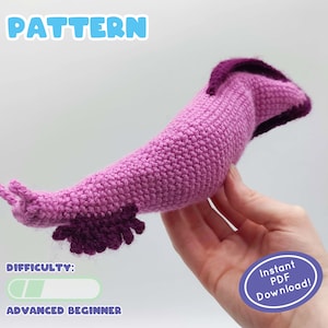May include: Crochet pattern for a pink and purple slug amigurumi toy. The pattern is labeled as "Advanced Beginner" in difficulty. The image shows the finished toy being held in a hand. The text "Instant PDF Download!" is also visible in the image.