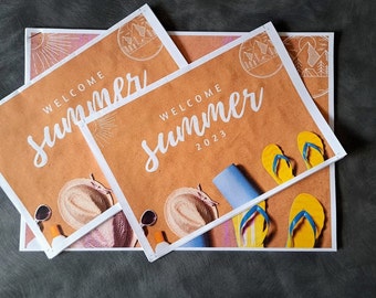 May include: Several square prints with a beach theme. The prints feature the words "WELCOME SUMMER 2023" in white script on a sand-colored background. Beach accessories like sunglasses, a hat, and flip-flops are also shown.