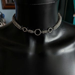 May include: A silver chain choker necklace with a large silver ring in the center.