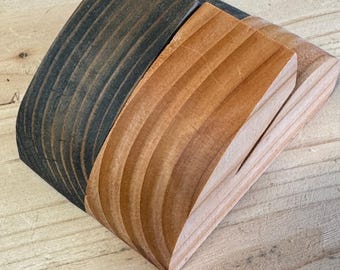 Puede incluir: Tres objetos de madera curvados en diferentes tonos de marrón. Los objetos están apilados, con la pieza más oscura en la parte inferior, seguida de un marrón medio y un marrón claro en la parte superior. La veta de la madera es visible.