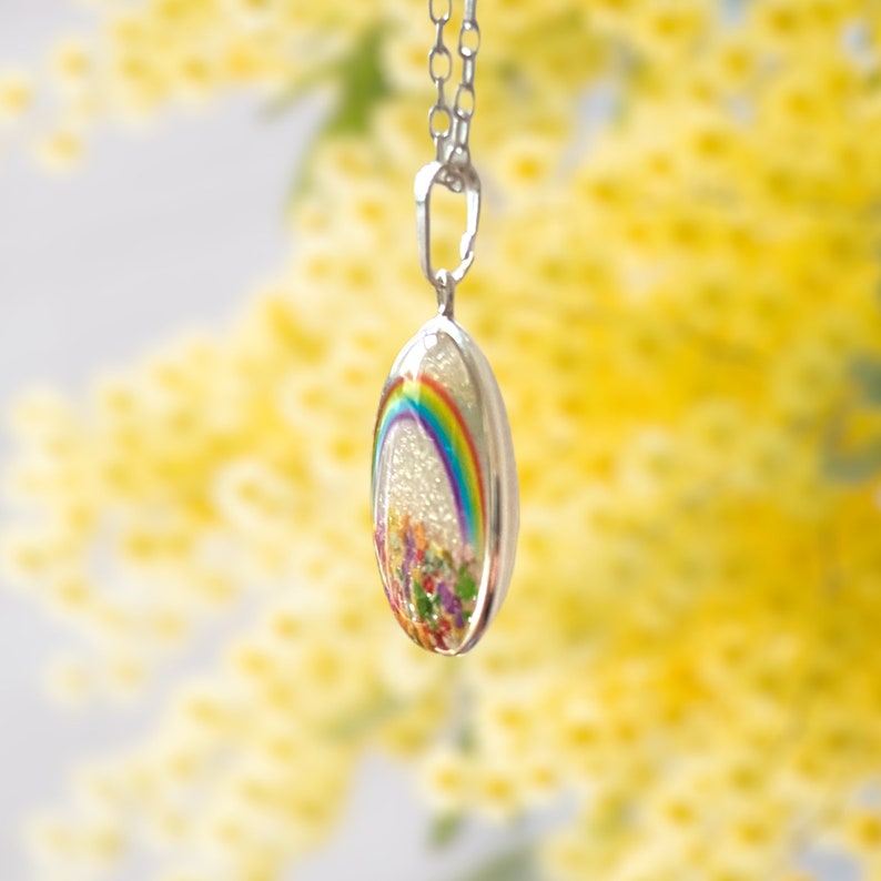 May include: A silver chain necklace with a clear oval pendant featuring a rainbow and colorful flowers inside.