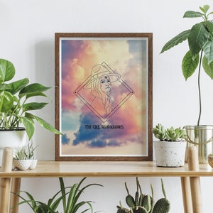 Peut inclure: Une impression encadrée avec un dessin au trait d'une personne portant un chapeau et un motif géométrique. L'arrière-plan est une aquarelle colorée de rose, bleu et jaune. Le texte "THE GIRL WHO KNOWS" est imprimé sous le dessin.