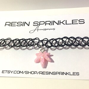 Op de afbeelding: Een zwarte choker ketting met een roze hars esdoornblad bedel. De bedel heeft een glinsterende afwerking. De ketting ligt op een witte kaart met de tekst "RESIN SPRINKLES Accessories" en "ETSY.COM/SHOP/RESINSPRINKLES".