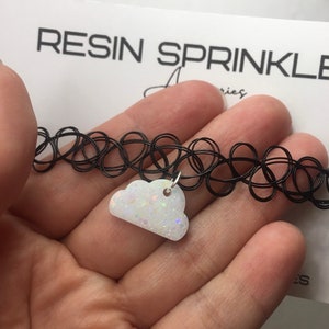 May include: A black choker necklace with a white cloud charm. The cloud charm is made of resin and has iridescent glitter embedded in it.