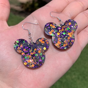 May include: A pair of black, orange, green, and purple glitter Mickey Mouse-shaped earrings with silver hooks.