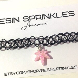 Op de afbeelding: Een zwarte choker ketting met een roze glitterhars esdoornblad bedel. De ketting ligt op een witte kaart met de tekst "RESIN SPRINKLES Accessories" en "ETSY.COM/SHOP/RESINSPRINKLES".