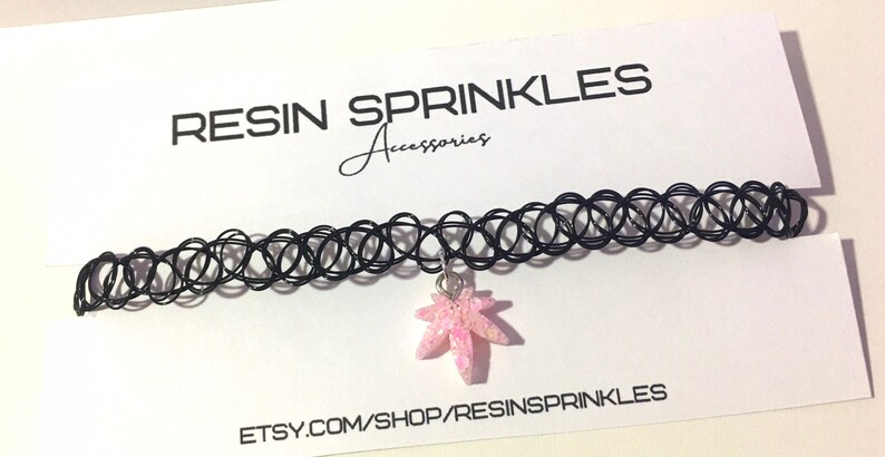 Op de afbeelding: Een zwarte choker ketting met een roze glitterhars esdoornblad bedel. De ketting ligt op een witte kaart met de tekst "RESIN SPRINKLES Accessories" en "ETSY.COM/SHOP/RESINSPRINKLES".