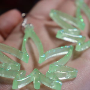 Peut inclure: Une paire de boucles d'oreilles en résine verte à paillettes en forme de feuilles de marijuana.