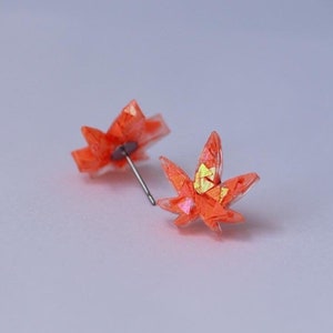 Peut inclure: Une paire de boucles d'oreilles clous en forme de feuille, de couleur orange et jaune irisé.