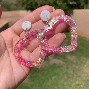 May include: Pink heart-shaped earrings with iridescent glitter and white round accents.