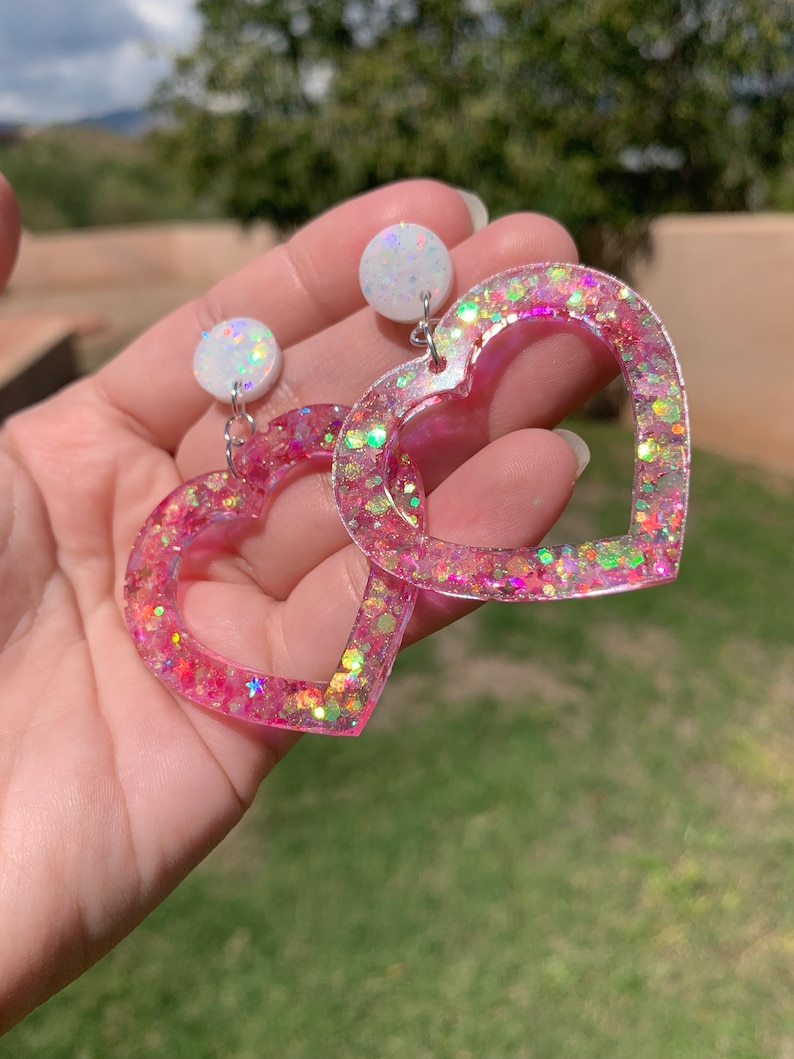 May include: Pink heart-shaped earrings with iridescent glitter and white round accents.