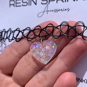 May include: A black choker necklace with a clear heart-shaped pendant filled with iridescent glitter.