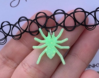 May include: A black choker necklace with a green glitter spider charm. The spider is a simple silhouette with eight legs.