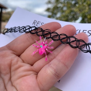 May include: A black choker necklace with a pink glitter spider charm.