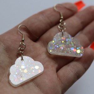May include: A pair of iridescent white cloud-shaped earrings with silver glitter. The earrings are on a silver chain with a hook closure.
