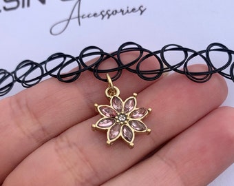 May include: A black choker necklace with a gold pendant shaped like a flower. The flower has pink petals and a small, clear gem in the center. The text "RESIN SPRINKLE Accessories" is visible in the background.