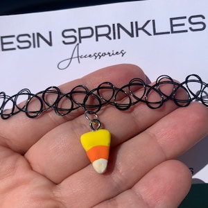 May include: Black choker necklace with a candy corn charm. The charm is made of yellow, orange, and white polymer clay.