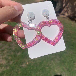 May include: Pink heart-shaped earrings with iridescent glitter and white opal-like accents.