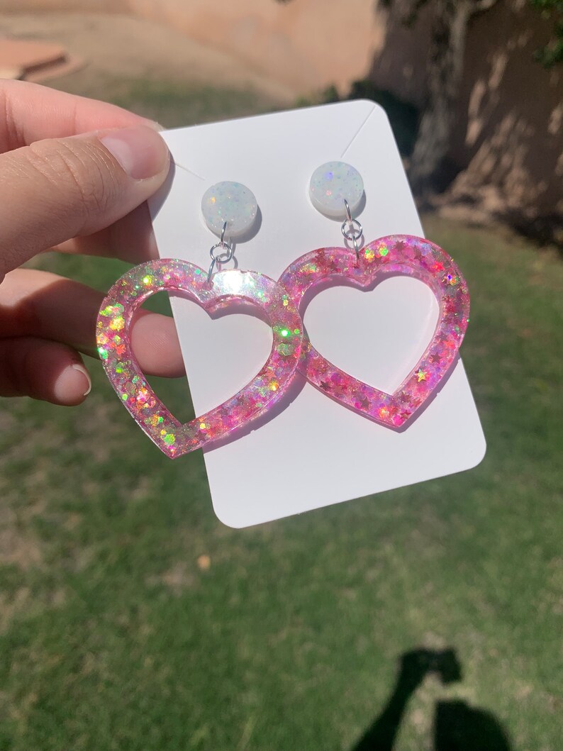May include: Pink heart-shaped earrings with iridescent glitter and white opal-like accents.