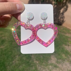 May include: Pink heart-shaped earrings with iridescent glitter and white opal-like tops.