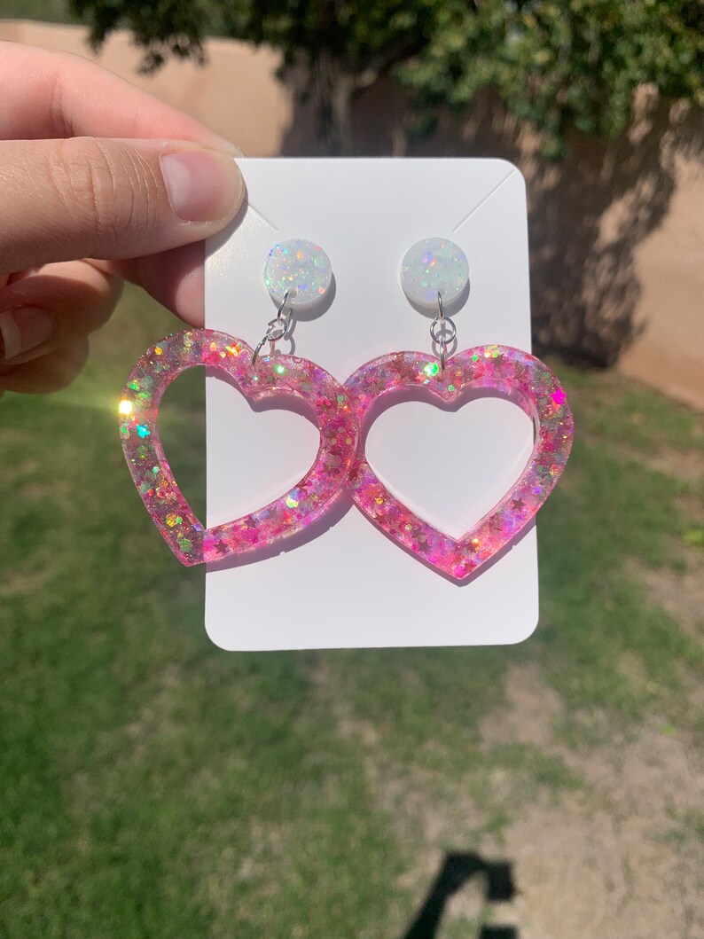 May include: Pink heart-shaped earrings with iridescent glitter and white opal-like tops.