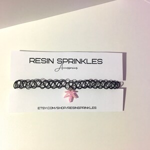 Op de afbeelding: Zwarte choker ketting met een roze hars blad hanger. De hanger is ingelegd met glitter. De ketting wordt getoond op een witte kaart met de tekst "RESIN SPRINKLES Accessories" en "ETSY.COM/SHOP/RESINSPRINKLES".