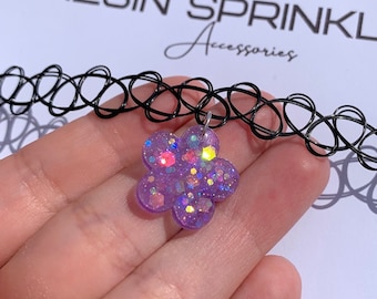 May include: A black choker necklace with a purple flower pendant. The flower pendant is made of resin and filled with glitter. The text "RESIN SPRINKLE Accessories" is visible in the background.