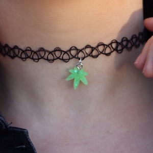 May include: A black choker necklace with a green marijuana leaf charm.