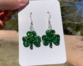 May include: A pair of green glitter shamrock dangle earrings with silver hooks.