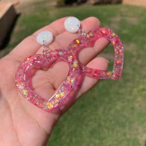 May include: A pair of pink heart-shaped earrings with iridescent glitter and white round accents.