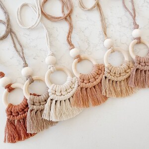 May include: A set of six macrame wall hangings with wooden rings and tassels in shades of brown, beige, and cream.