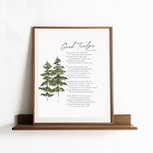 Puede incluir: Una impresión enmarcada con el poema "Good Timber" de Douglas Malloch. La obra de arte incluye una ilustración en acuarela de árboles de hoja perenne en tonos verdes. La impresión se muestra en una estantería de madera.