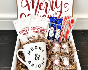 May include: White gift box with a red "Merry" inscription. The box contains a white mug with black "Merry & Bright" text, two packages of Swiss Miss hot chocolate mix, two snowman-shaped marshmallow treats, four peppermint candies, and two red and white candy canes.