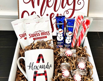 May include: A white mug with a red and black plaid letter A and the name "Alexandra" printed on it. The mug is in a white gift box with brown shredded paper. The box also contains hot chocolate packets, candy canes, and marshmallow treats.