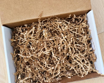 May include: A cardboard box filled with brown packing paper shreds. The box is open and the shreds are visible.