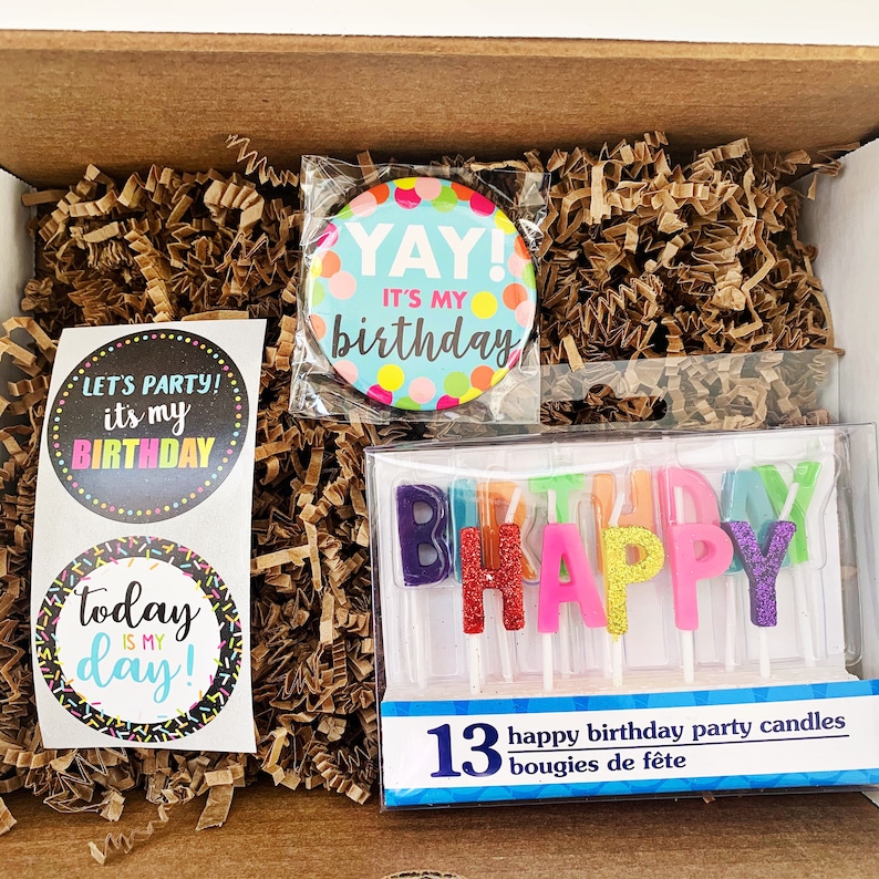 Może przedstawiać: Pudełko prezentowe na przyjęcie urodzinowe z niebieskim i białym guzikiem z napisem "YAY! It's my birthday", dwie naklejki z napisami "Let's party! It's my birthday" i "Today is my day!" oraz opakowanie 13 kolorowych świeczek, kt&oacute;re tworzą napis "HAPPY".