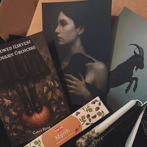 May include: An assortment of occult items, including a book titled "Shadowed Harvest", incense, candles, and art prints. The art prints depict a woman with a raven and a goat. The incense box reads "Myrrh Premium Masala Incense".
