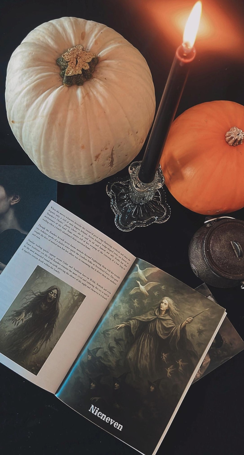 May include: A still life featuring a white pumpkin, an orange pumpkin, a lit black candle in a glass holder, and an open book with illustrations. The book's title is "Nicneven". The scene is set on a dark surface.