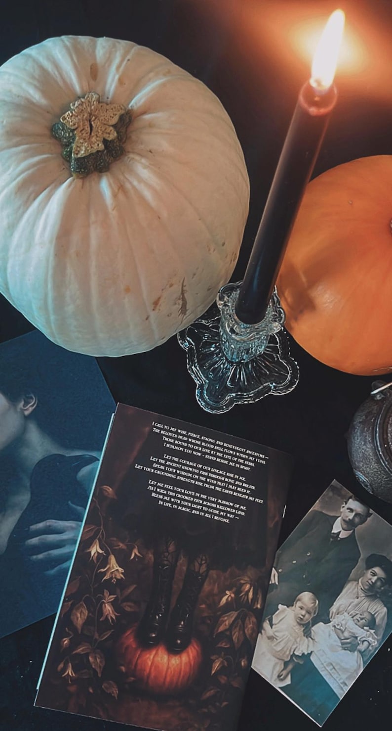May include: A still-life arrangement featuring a white pumpkin, an orange pumpkin, a lit black candle in a glass holder, and vintage photographs. A book with gothic illustrations and text is also present, creating a Halloween or autumn theme.