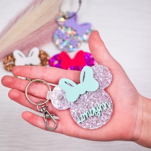 May include: A silver glitter mouse-shaped keychain with a light blue bow and the name "Imayn" written in pink glitter.