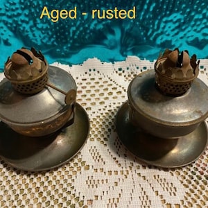May include: Two antique oil lamps with a rusted finish and ornate metal tops. The lamps are sitting on a white lace doily.