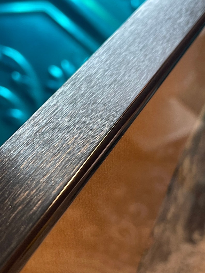 May include: Close-up of a dark gray picture frame with a brushed metal finish. The frame has a thin black border.