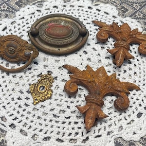May include: Five antique metal drawer pulls and decorative accents. The pulls are made of brass and have a tarnished finish. The accents are made of iron and have a rusty finish.