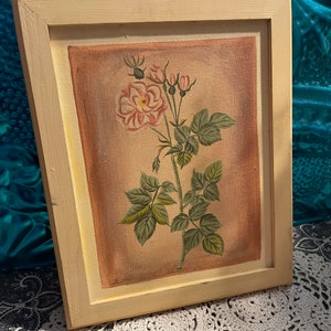 Puede incluir: Una pintura enmarcada de una sola rosa rosa con hojas verdes y capullos sobre un fondo beige. El marco es de madera beige claro.
