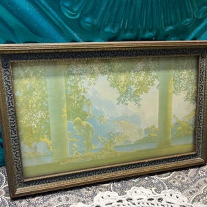 May include: A vintage framed print of a landscape scene with trees, mountains, and a river. The print is in a gold-colored frame with a decorative border.