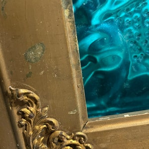 K&ouml;nnte beinhalten: Ein goldfarbener Bilderrahmen mit verzierten Details. Der Rahmen hat einen Einsatz aus t&uuml;rkisfarbenem Glas.