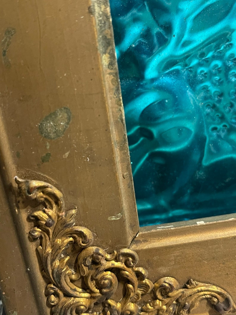 K&ouml;nnte beinhalten: Ein goldfarbener Bilderrahmen mit verzierten Details. Der Rahmen hat einen Einsatz aus t&uuml;rkisfarbenem Glas.